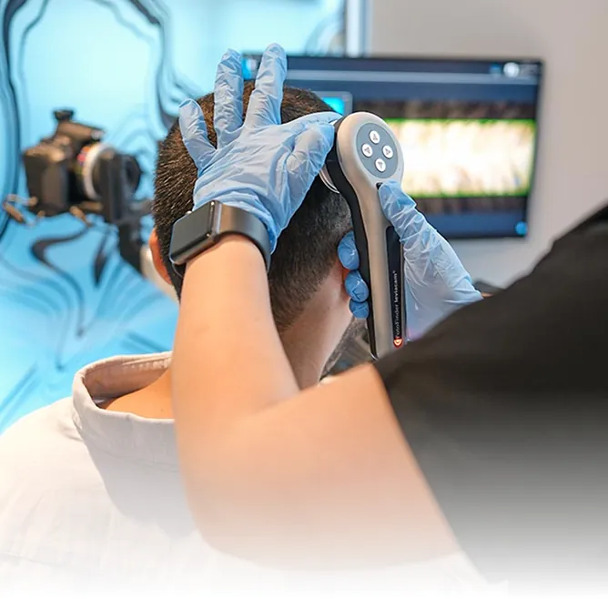 A medical professional wearing blue gloves using a FotoFinder Leviacam hand-held device to conduct a detailed scalp and hair follicle analysis on a patient
